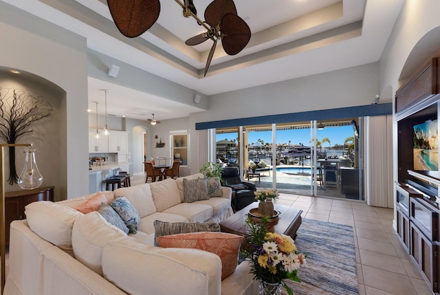 living area featuring arched walkways, a raised ceiling, ceiling fan, and light tile patterned flooring