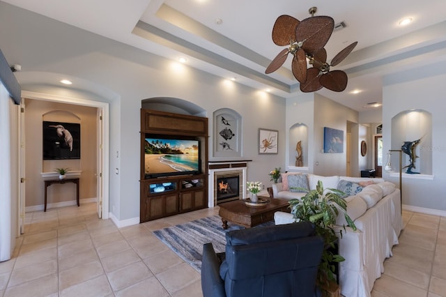 living room featuring ceiling fan, a glass covered fireplace, baseboards, and light tile patterned floors