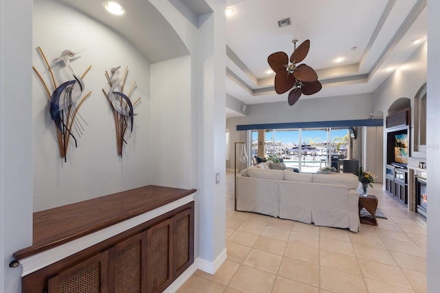 living room featuring a tray ceiling, baseboards, visible vents, ceiling fan, and light tile patterned flooring