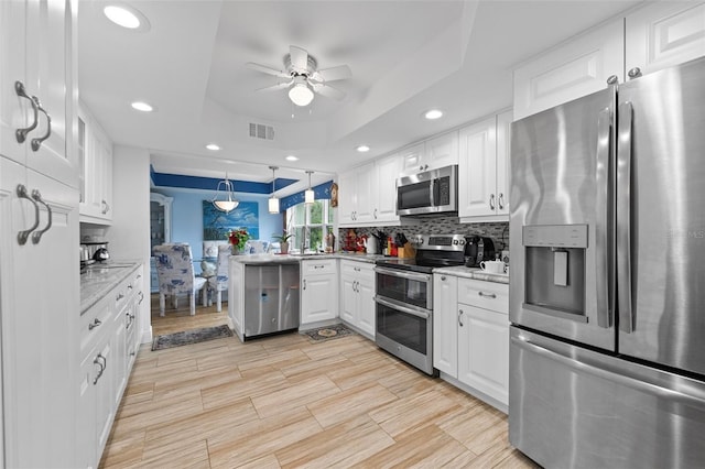 kitchen with visible vents, a tray ceiling, appliances with stainless steel finishes, a peninsula, and a ceiling fan