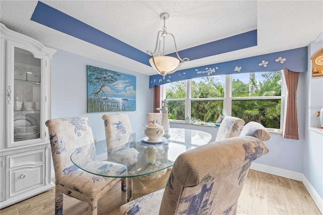 dining space featuring a raised ceiling, baseboards, light wood finished floors, and a textured ceiling