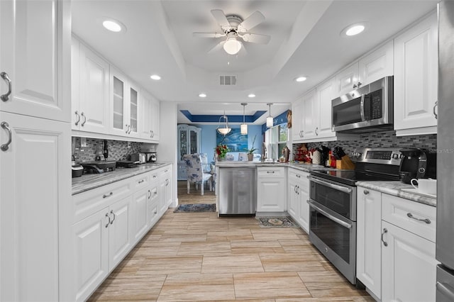 kitchen featuring a peninsula, stainless steel appliances, white cabinetry, a raised ceiling, and a ceiling fan