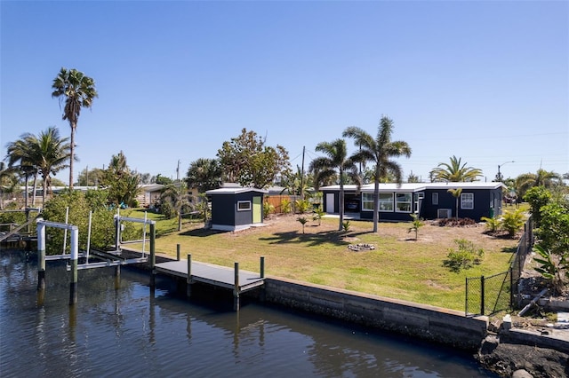 dock area with boat lift, a lawn, fence, and a water view