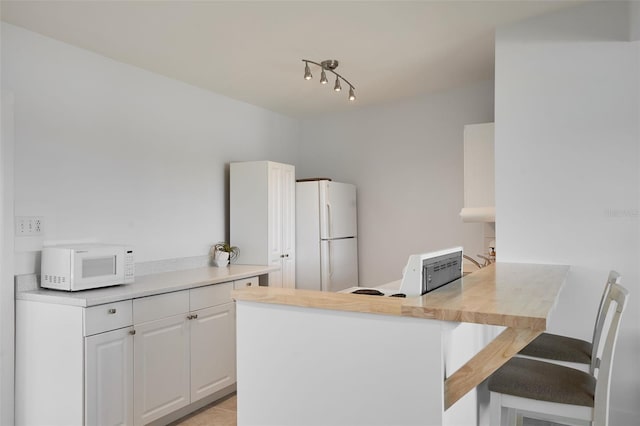 kitchen with white cabinetry, white appliances, a peninsula, a breakfast bar area, and light countertops