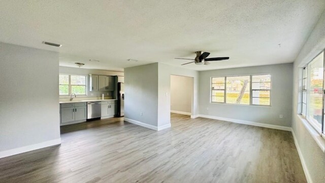 unfurnished living room with a ceiling fan, wood finished floors, baseboards, and a textured ceiling