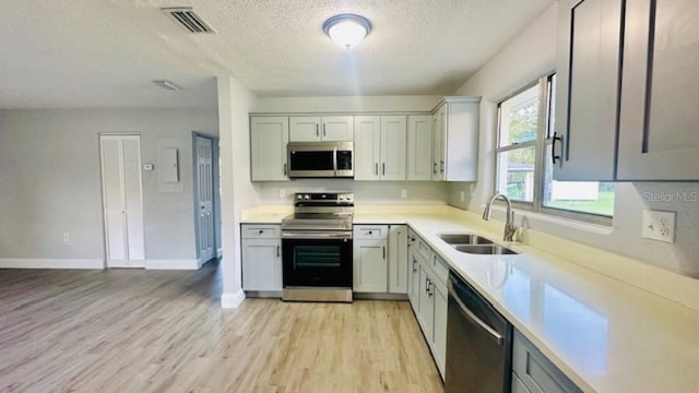 kitchen featuring visible vents, a sink, stainless steel appliances, light countertops, and light wood-type flooring