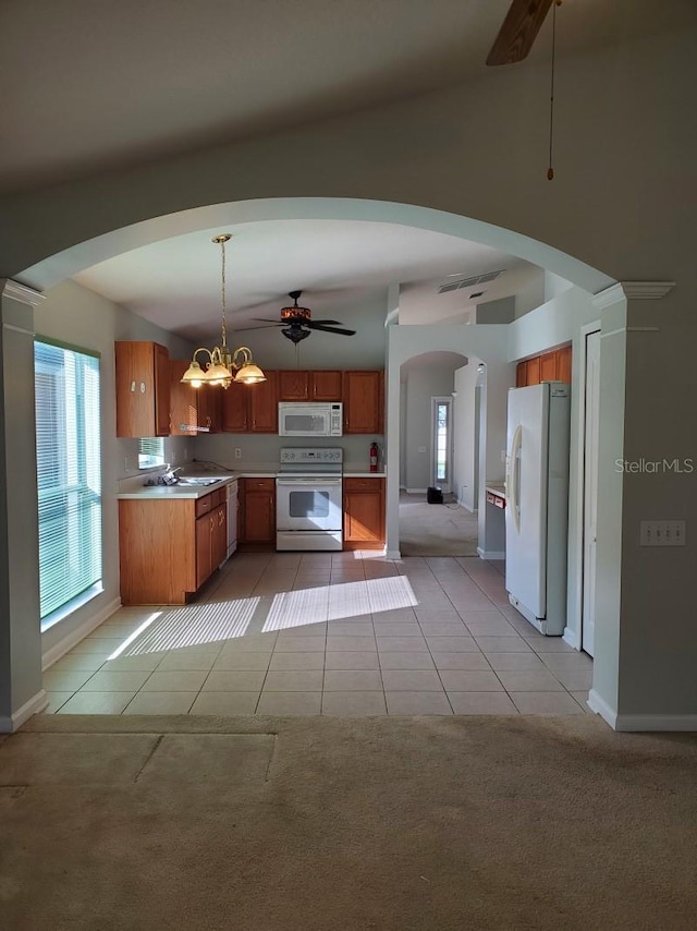 kitchen with brown cabinets, white appliances, arched walkways, light tile patterned flooring, and light colored carpet