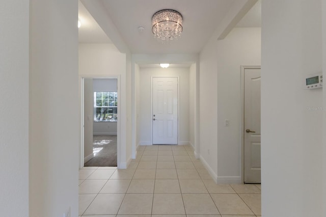 hall featuring light tile patterned floors, baseboards, and an inviting chandelier