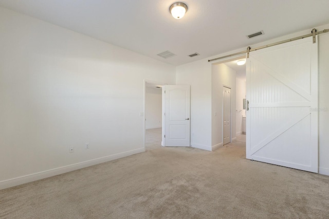 empty room with a barn door, light carpet, and visible vents