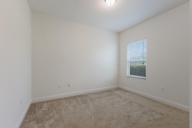 spare room featuring light carpet and baseboards