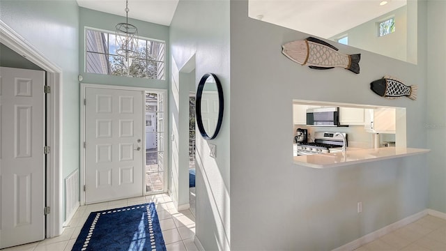 foyer entrance featuring a chandelier, baseboards, a towering ceiling, and light tile patterned flooring