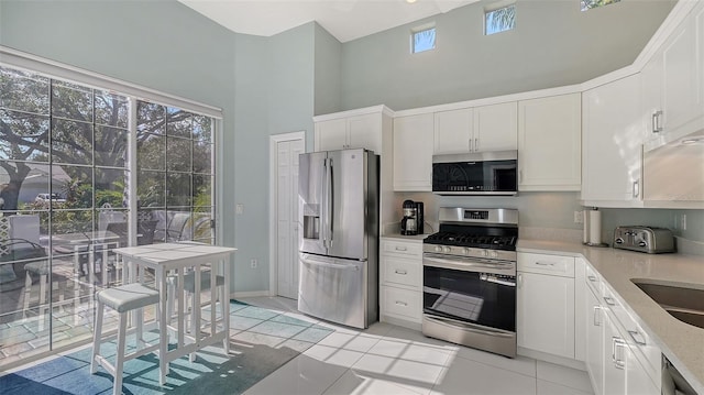 kitchen with light tile patterned floors, stainless steel appliances, a high ceiling, plenty of natural light, and white cabinetry