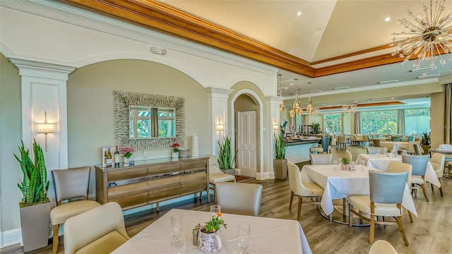 dining room with a notable chandelier, wood finished floors, ornate columns, and ornamental molding