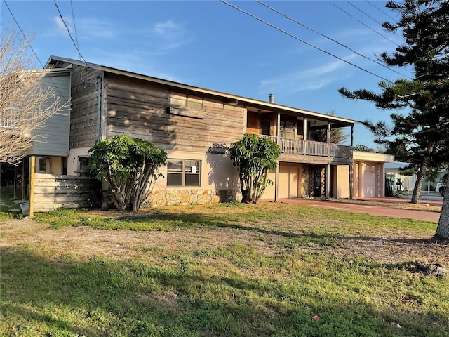 rear view of house with a balcony, a yard, an attached garage, stucco siding, and stone siding