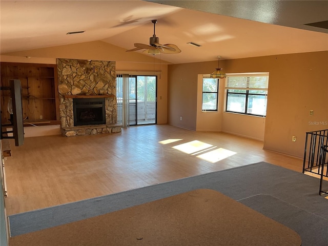 unfurnished living room with a stone fireplace, lofted ceiling, wood finished floors, and visible vents