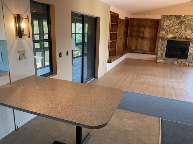 unfurnished living room featuring a stone fireplace, vaulted ceiling, built in shelves, and wood finished floors