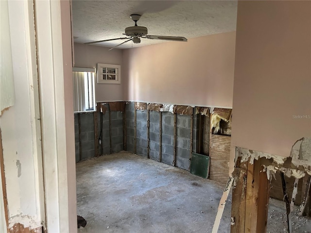 interior space featuring a textured ceiling, concrete block wall, unfinished concrete flooring, and ceiling fan