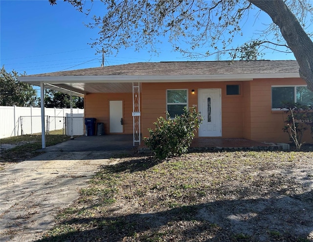 ranch-style home with concrete driveway, fence, roof with shingles, and a carport