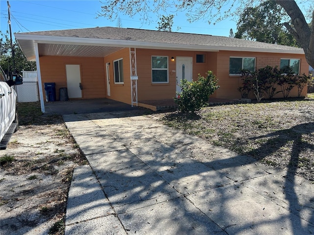 ranch-style home with a carport, fence, driveway, and roof with shingles