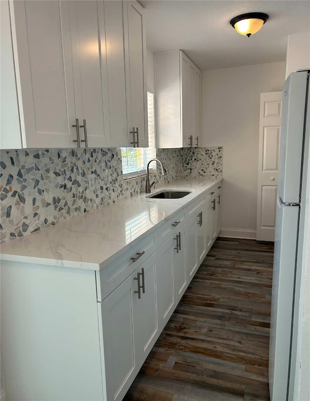 kitchen featuring dark wood-style floors, freestanding refrigerator, a sink, white cabinets, and tasteful backsplash