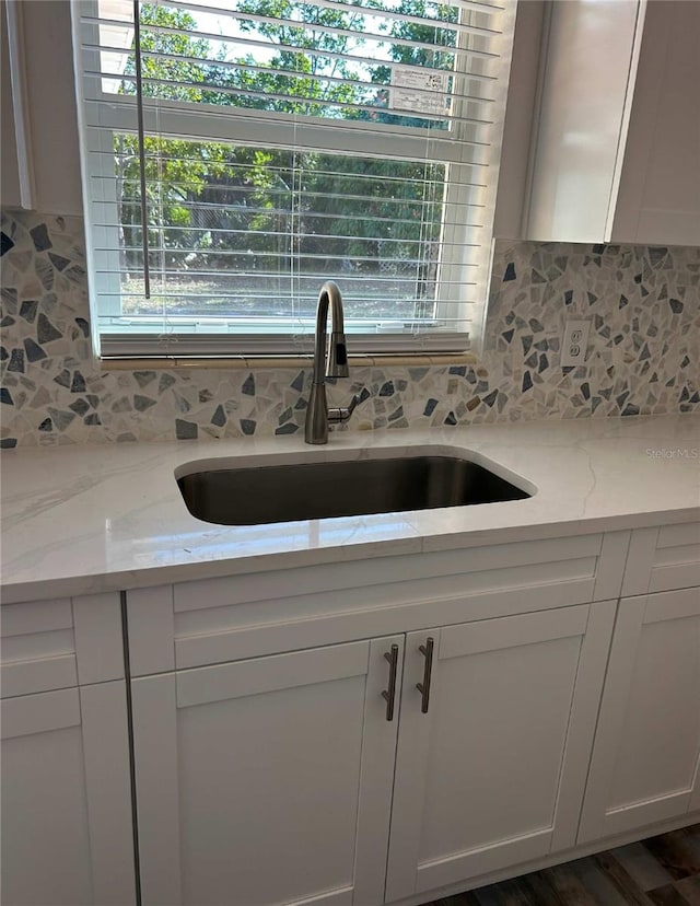 kitchen featuring tasteful backsplash, white cabinetry, light stone counters, and a sink