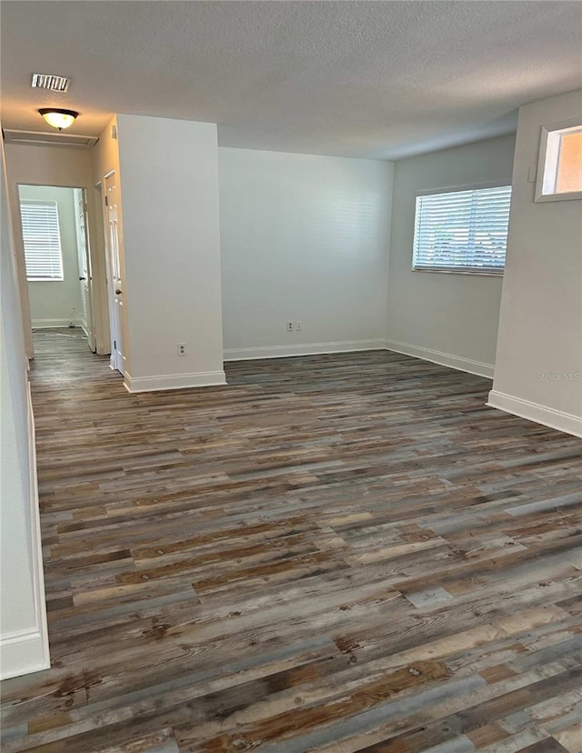 spare room featuring visible vents, baseboards, dark wood-type flooring, and a textured ceiling