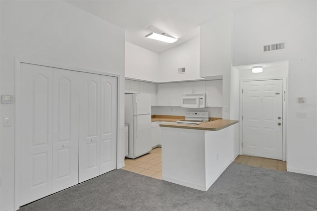 kitchen featuring light carpet, visible vents, white appliances, and a peninsula