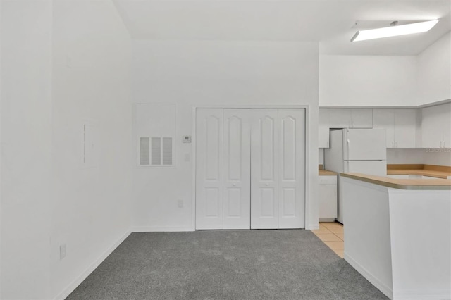 kitchen featuring visible vents, a high ceiling, freestanding refrigerator, white cabinets, and light colored carpet