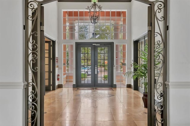 tiled entryway featuring a wealth of natural light, french doors, an inviting chandelier, and a towering ceiling