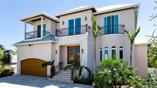 view of front facade featuring stucco siding, driveway, french doors, an attached garage, and a balcony