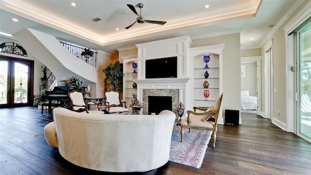 living area with dark wood-style floors, visible vents, a raised ceiling, and a ceiling fan