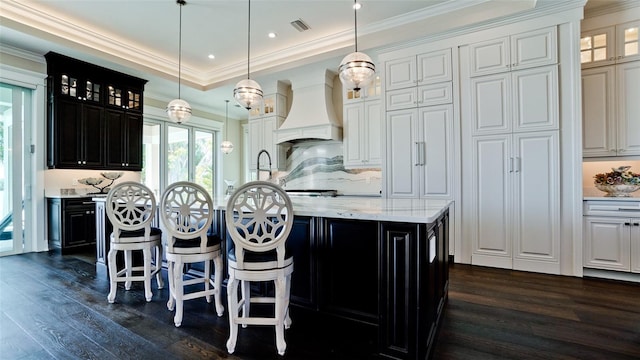 kitchen with visible vents, dark wood-type flooring, ornamental molding, custom range hood, and a tray ceiling