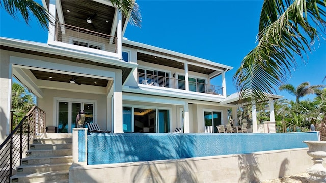 back of house with stucco siding, stairs, a balcony, and ceiling fan