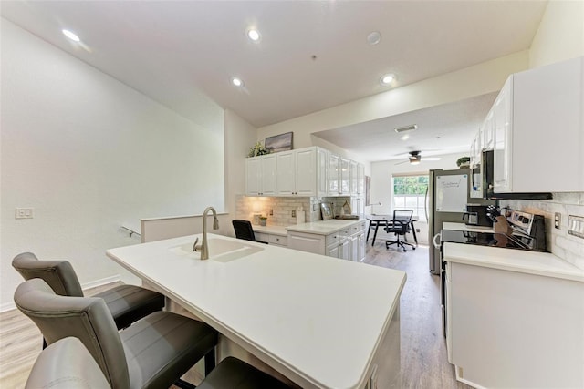 kitchen featuring light wood-style flooring, a kitchen island with sink, a sink, white cabinets, and tasteful backsplash