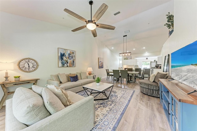 living area with baseboards, visible vents, high vaulted ceiling, ceiling fan, and light wood-style floors