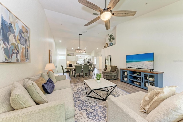 living room featuring visible vents, ceiling fan with notable chandelier, high vaulted ceiling, and light wood-style flooring