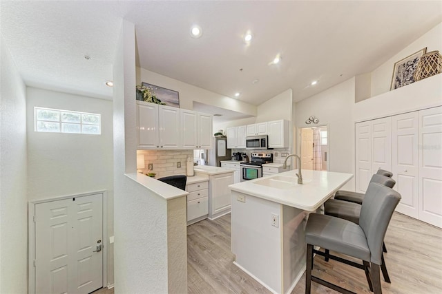 kitchen with light wood-style flooring, light countertops, appliances with stainless steel finishes, white cabinetry, and a kitchen breakfast bar