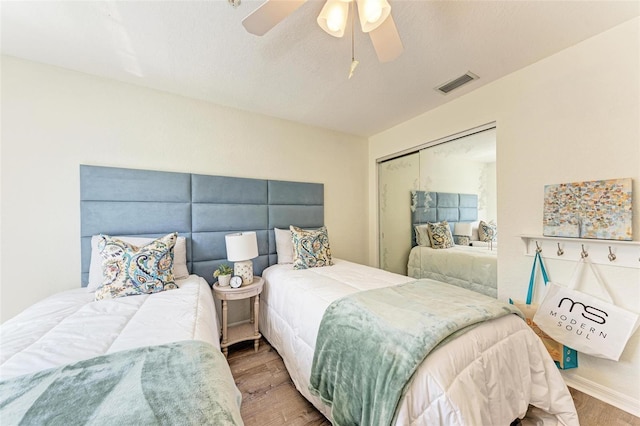 bedroom with a ceiling fan, wood finished floors, visible vents, and a closet