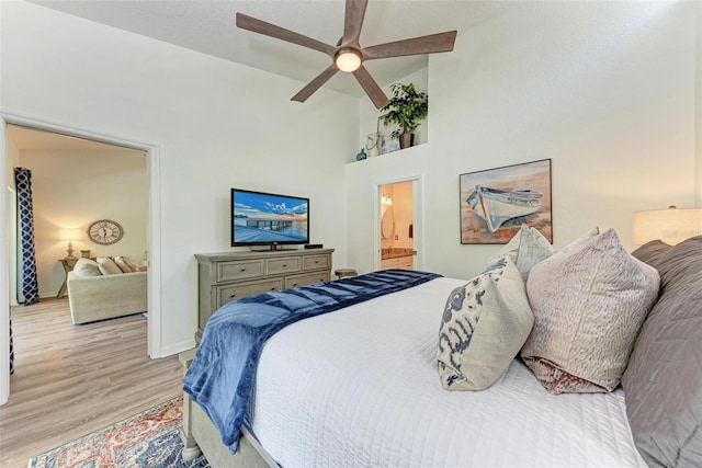 bedroom with light wood-style flooring, a ceiling fan, ensuite bathroom, baseboards, and a towering ceiling