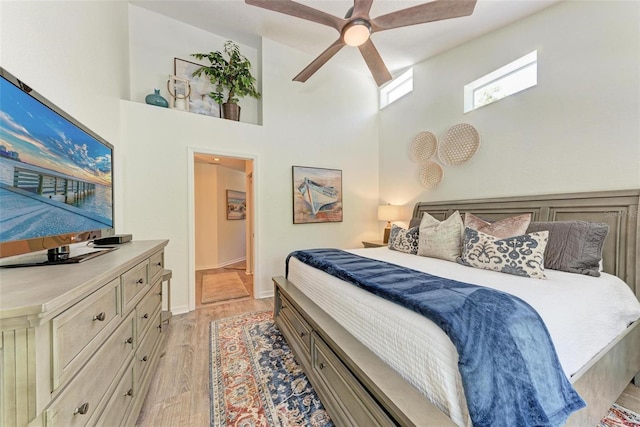 bedroom featuring ceiling fan, light wood-style flooring, and a towering ceiling