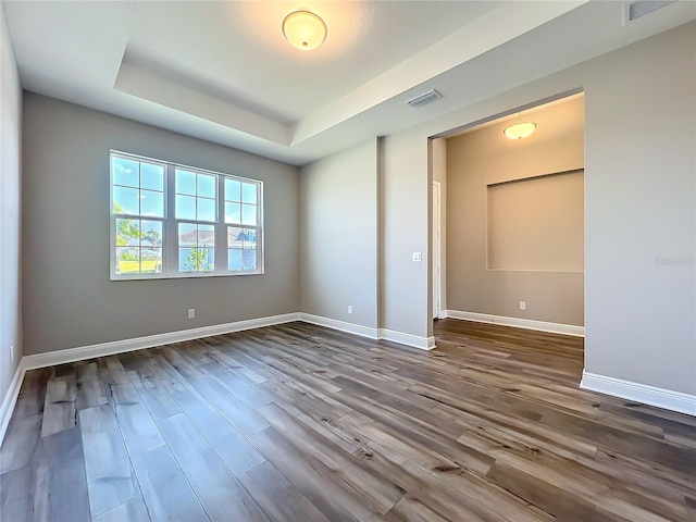 unfurnished bedroom featuring visible vents, a raised ceiling, baseboards, and wood finished floors