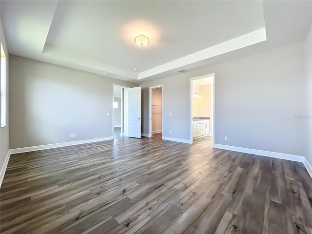 unfurnished bedroom with a walk in closet, a raised ceiling, wood finished floors, a closet, and baseboards