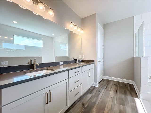 full bath featuring double vanity, wood finished floors, baseboards, and a sink