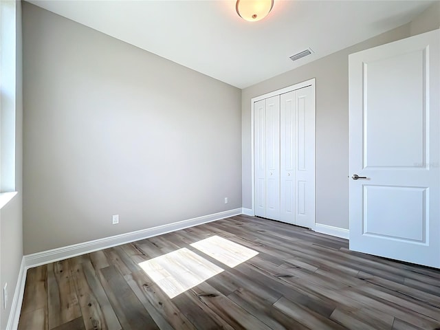 unfurnished bedroom featuring a closet, baseboards, visible vents, and wood finished floors