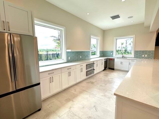 kitchen featuring light stone countertops, visible vents, decorative backsplash, stainless steel appliances, and a sink