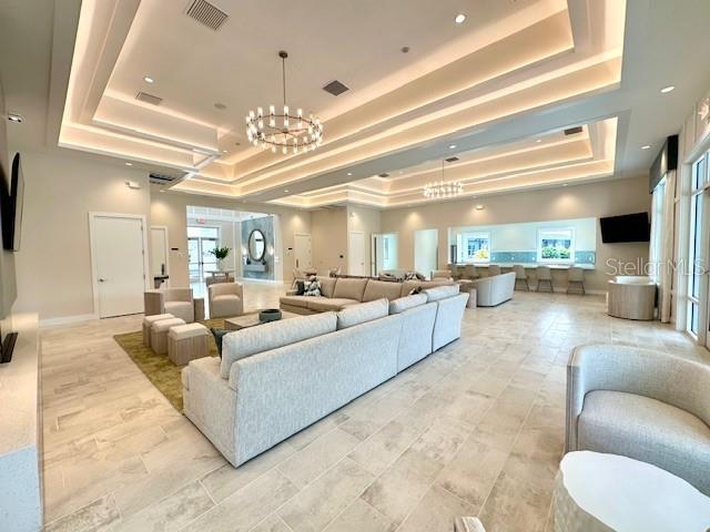 living room with visible vents, baseboards, a raised ceiling, and an inviting chandelier