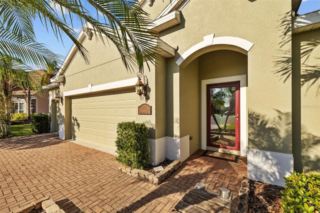 property entrance featuring stucco siding, decorative driveway, and an attached garage