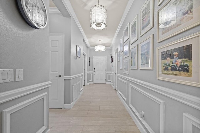 corridor featuring a decorative wall, crown molding, an inviting chandelier, and a wainscoted wall