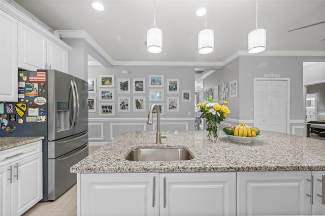 kitchen with ornamental molding, a sink, stainless steel refrigerator with ice dispenser, white cabinetry, and a decorative wall