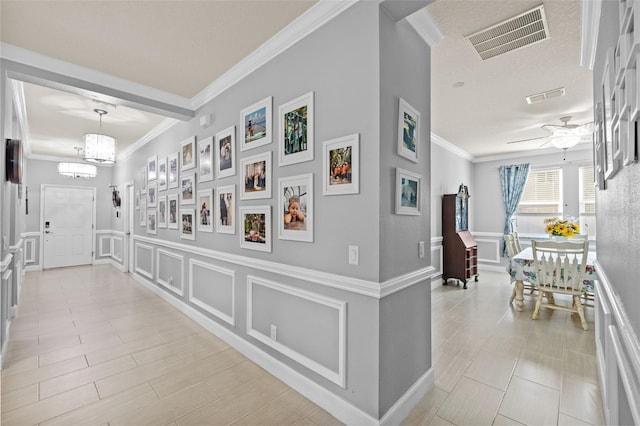 corridor featuring visible vents, an inviting chandelier, crown molding, and a decorative wall